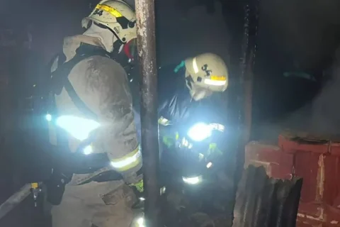 Двоє пожежників у касках працюють у задимленому згорілому будинку